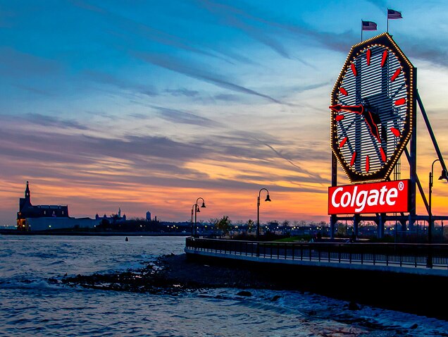 ακτή της θάλασσας, το λογότυπο της Colgate στο βάθος, κάτω από ένα μεγάλο ρολόι με κόκκινα δείκτες