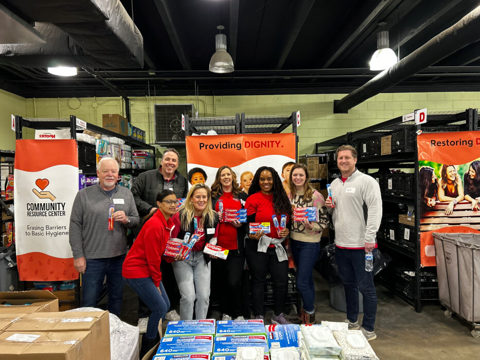 Group of Colgate employee volunteers posing with hygiene product donations at a Community Resource Center warehouse event.
